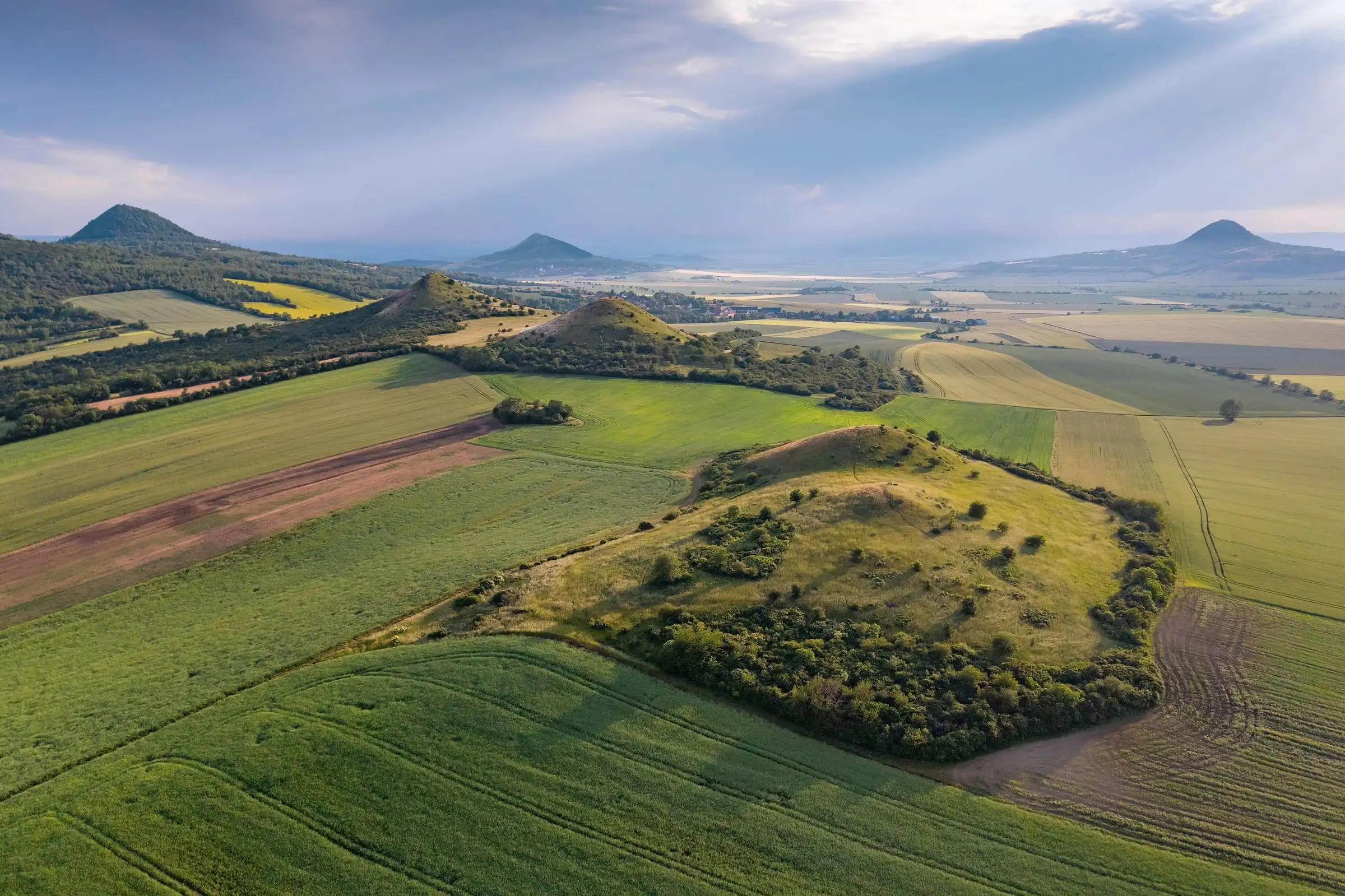 Letecký pohled na kopce Českého středohoří po dešti: pole a sopečné kužely.